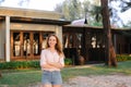 Young woman standing near resort house, wearing jeans shorts and blouse. Royalty Free Stock Photo