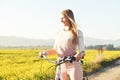 Young woman standing next to her bike over dusty country road, strong afternoon sun backlight in background shines on yellow