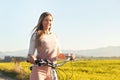 Young woman standing next to her bike over dusty country road, strong afternoon sun backlight in background shines on yellow Royalty Free Stock Photo