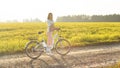 Young woman standing next to her electric bike over dusty country road, strong afternoon sun backlight in background shines on Royalty Free Stock Photo