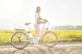 Young woman standing next to her electric bike over dusty country road, strong afternoon sun backlight in background shines on