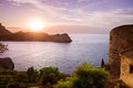 A young woman standing at an old castle on Mallorca with a view of an island in the Spanish Mediterranean Sea at a romantic sunset