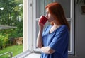 young woman looking out of window while drinking from coffee cup Royalty Free Stock Photo