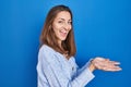 Young woman standing over blue background pointing aside with hands open palms showing copy space, presenting advertisement Royalty Free Stock Photo