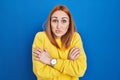 Young woman standing over blue background shaking and freezing for winter cold with sad and shock expression on face Royalty Free Stock Photo