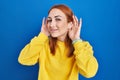 Young woman standing over blue background trying to hear both hands on ear gesture, curious for gossip