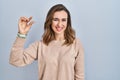 Young woman standing over isolated background smiling and confident gesturing with hand doing small size sign with fingers looking Royalty Free Stock Photo