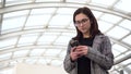 A young woman is standing with a phone. A girl uses a smartphone against a pan-glass roof. A busy person is texting in Royalty Free Stock Photo