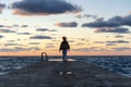 Young woman standing on a pier near the water in the sunset rays against the backdrop of beautiful bright clouds Royalty Free Stock Photo