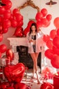 Young woman standing in room filled with mix of red balloons. Girl holding glass of champagne Royalty Free Stock Photo