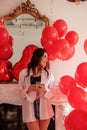 Young woman standing in room filled with mix of red balloons. Girl holding glass of champagne Royalty Free Stock Photo