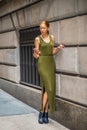 Young woman standing on street by wall in New York City, texting on cell phone Royalty Free Stock Photo