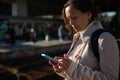 Young woman standing on the train station railway platform, checking her mobile phone white waiting to board the train Royalty Free Stock Photo