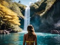 young woman standing in tropical blue lake looking at waterfall landscape Royalty Free Stock Photo