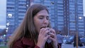 Young woman standing in an urban street and eating burger. Young woman eating fast food standing on the street