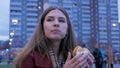 Young woman standing in an urban street and eating burger. Young woman eating fast food standing on the street