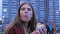 Young woman standing in an urban street and eating burger. Young woman eating fast food standing on the street