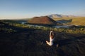 A young woman is standing in a yoga pose against the beautiful nature landscape of valley, volcanic lake and crater