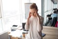 Young woman stands in a big office room and keeping her hands close to the head. She has a headache. It is a strong pain