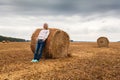 A young woman stands on the field, leaning on a sheaf of hay. Royalty Free Stock Photo