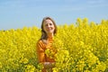 A young woman stands in a flowering rapeseed field. Summer