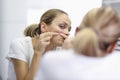 Young woman stands in front of mirror and presses pimples with hands portrait