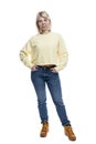 A young woman stands in full growth. Smiling blonde in a yellow sweater and jeans. Isolated on white background. Vertical