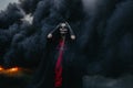 Woman stands in Halloween costume of death against background of fire, flame and black smoke