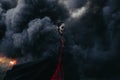 Woman stands in Halloween costume of death against background of fire, flame and black smoke