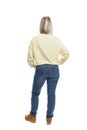 A young woman stands with her back in full growth. Smiling blonde in a yellow sweater and jeans. Isolated on white background.