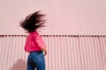 Young woman stands her back to camera and waving her long straight dark hair on pink background. Female with flying hair in pink Royalty Free Stock Photo