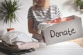 Young woman stands indoor at table and holds a box with things for donation . Clothes Donation, Renewable Concept and reuse