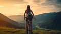 Young woman stands with sports bike on mountain trail at sunset, back view of female person on bicycle looking at landscape. Royalty Free Stock Photo