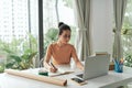 A young woman starting an online business works on her laptop and waits for orders