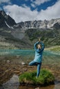 Young woman stays in one leg yoga position against the turquoise lake in the mountains Royalty Free Stock Photo