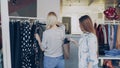 Young woman stealing wallet from female customer choosing clothes in shop. Royalty Free Stock Photo