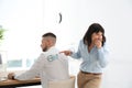 Woman sticking paper fish to colleague`s back in office. April fool`s day