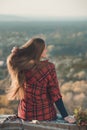 Young woman straightens a long hair sits on a hill overlooking the village. Back view Royalty Free Stock Photo