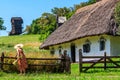 Young woman in straw hat collects flowers near ancient traditional ukrainian rural house