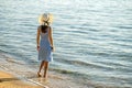 Young woman in straw hat and a dress standing alone on empty sand beach at sea shore. Lonely tourist girl looking at horizon over Royalty Free Stock Photo