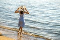 Young woman in straw hat and a dress standing alone on empty sand beach at sea shore. Lonely tourist girl looking at horizon over Royalty Free Stock Photo