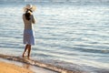 Young woman in straw hat and a dress standing alone on empty sand beach at sea shore. Lonely tourist girl looking at horizon over Royalty Free Stock Photo