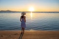 Young woman in straw hat and a dress standing alone on empty sand beach at sunset sea shore. Lonely girl looking at horizon over Royalty Free Stock Photo