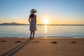 Young woman in straw hat and a dress standing alone on empty sand beach at sunset sea shore. Lonely girl looking at horizon over Royalty Free Stock Photo