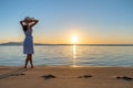 Young woman in straw hat and a dress standing alone on empty sand beach at sunset sea shore. Lonely girl looking at horizon over Royalty Free Stock Photo