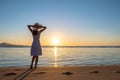 Young woman in straw hat and a dress standing alone on empty sand beach at sunset sea shore. Lonely girl looking at horizon over Royalty Free Stock Photo