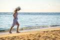 Young woman in straw hat and a dress walking alone on empty sand beach at sea shore. Lonely tourist girl looking at horizon over Royalty Free Stock Photo