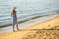 Young woman in straw hat and a dress walking alone on empty sand beach at sea shore. Lonely tourist girl looking at horizon over Royalty Free Stock Photo