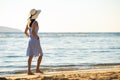 Young woman in straw hat and a dress walking alone on empty sand beach at sea shore. Lonely tourist girl looking at horizon over Royalty Free Stock Photo