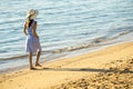 Young woman in straw hat and a dress walking alone on empty sand beach at sea shore. Lonely tourist girl looking at horizon over Royalty Free Stock Photo